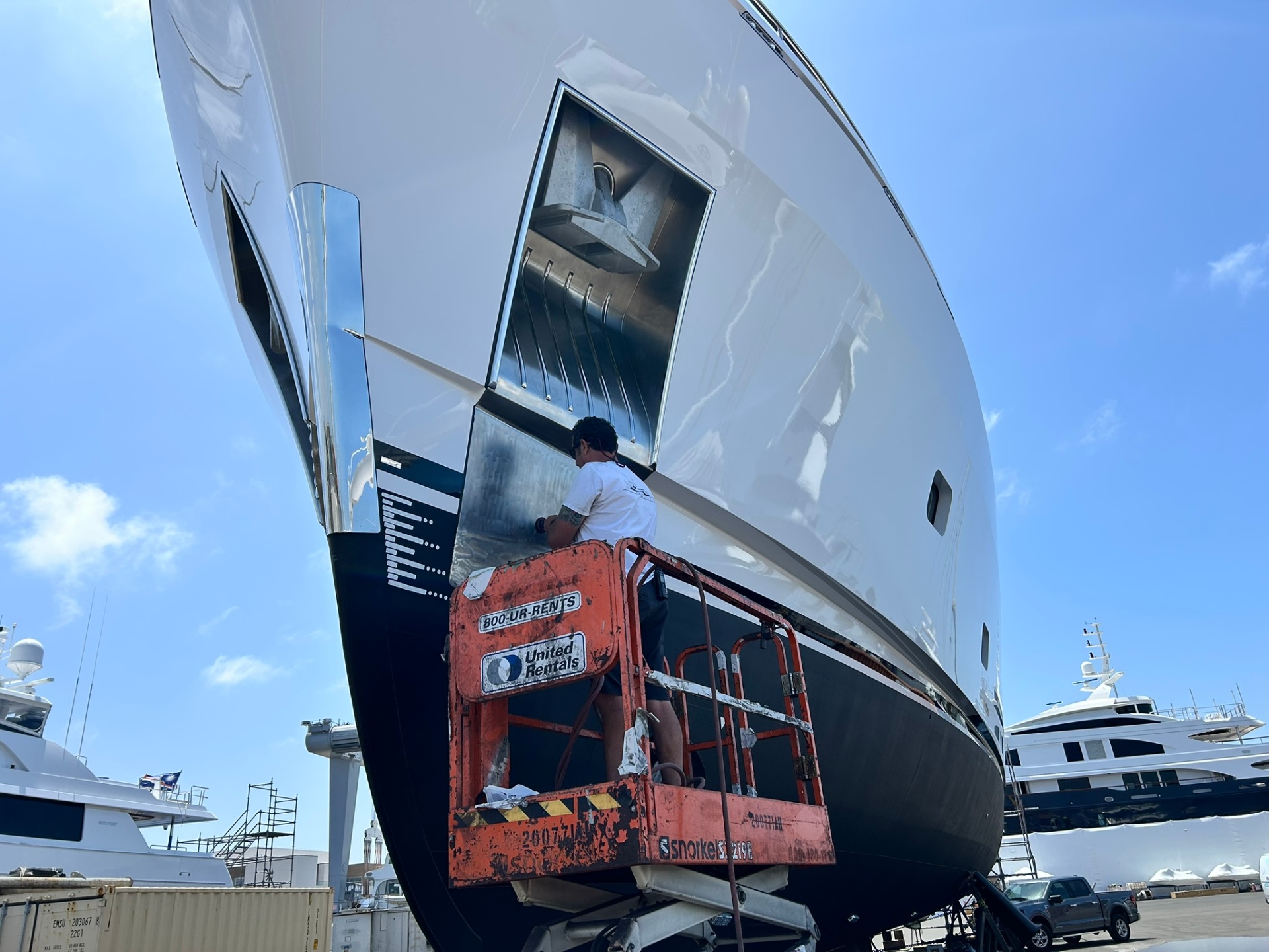 Worker on a lift performing exterior refit work on a large yacht hull.